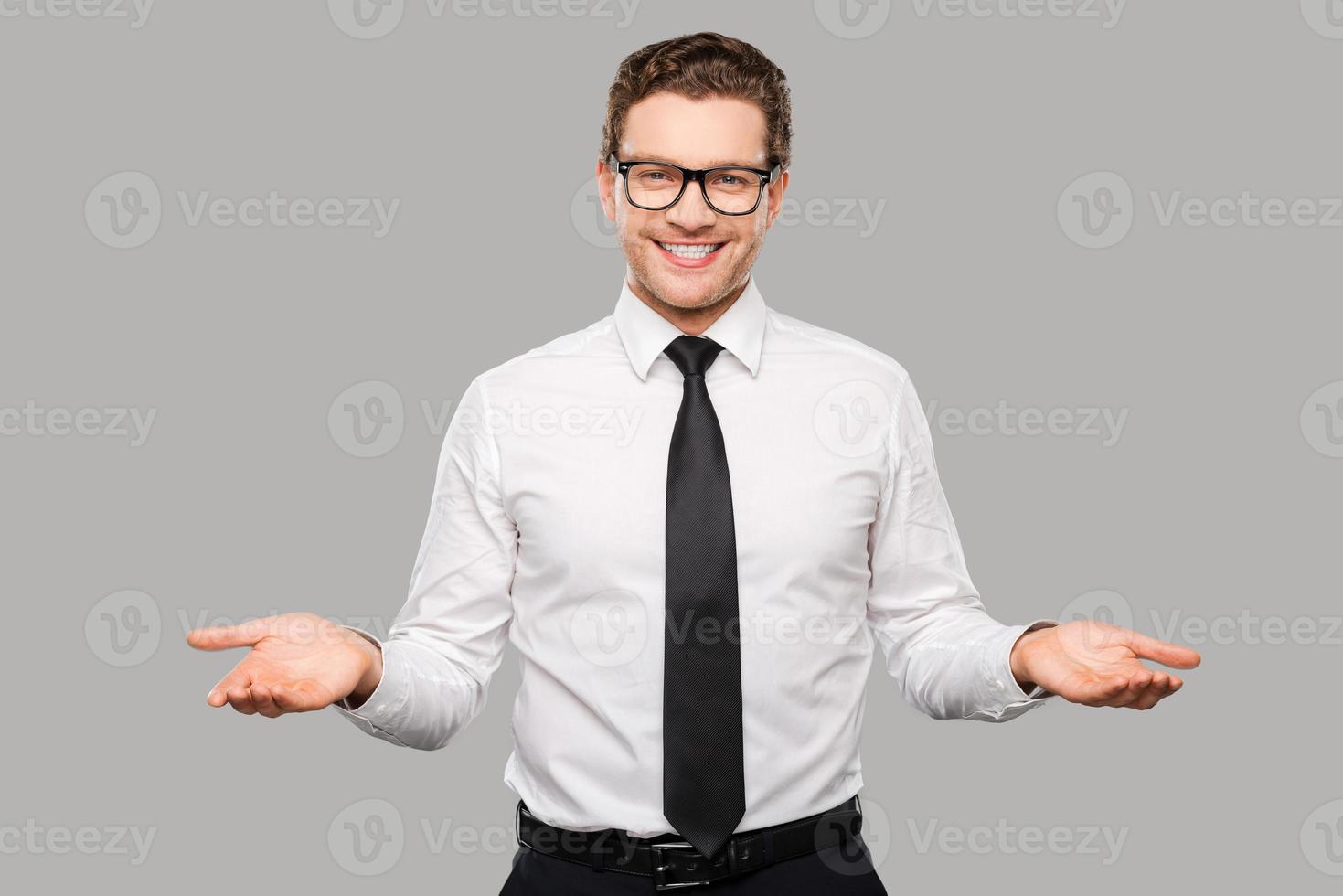 Welcome on board Handsome young man in shirt and tie stretching out his arms and smiling while standing against grey background photo