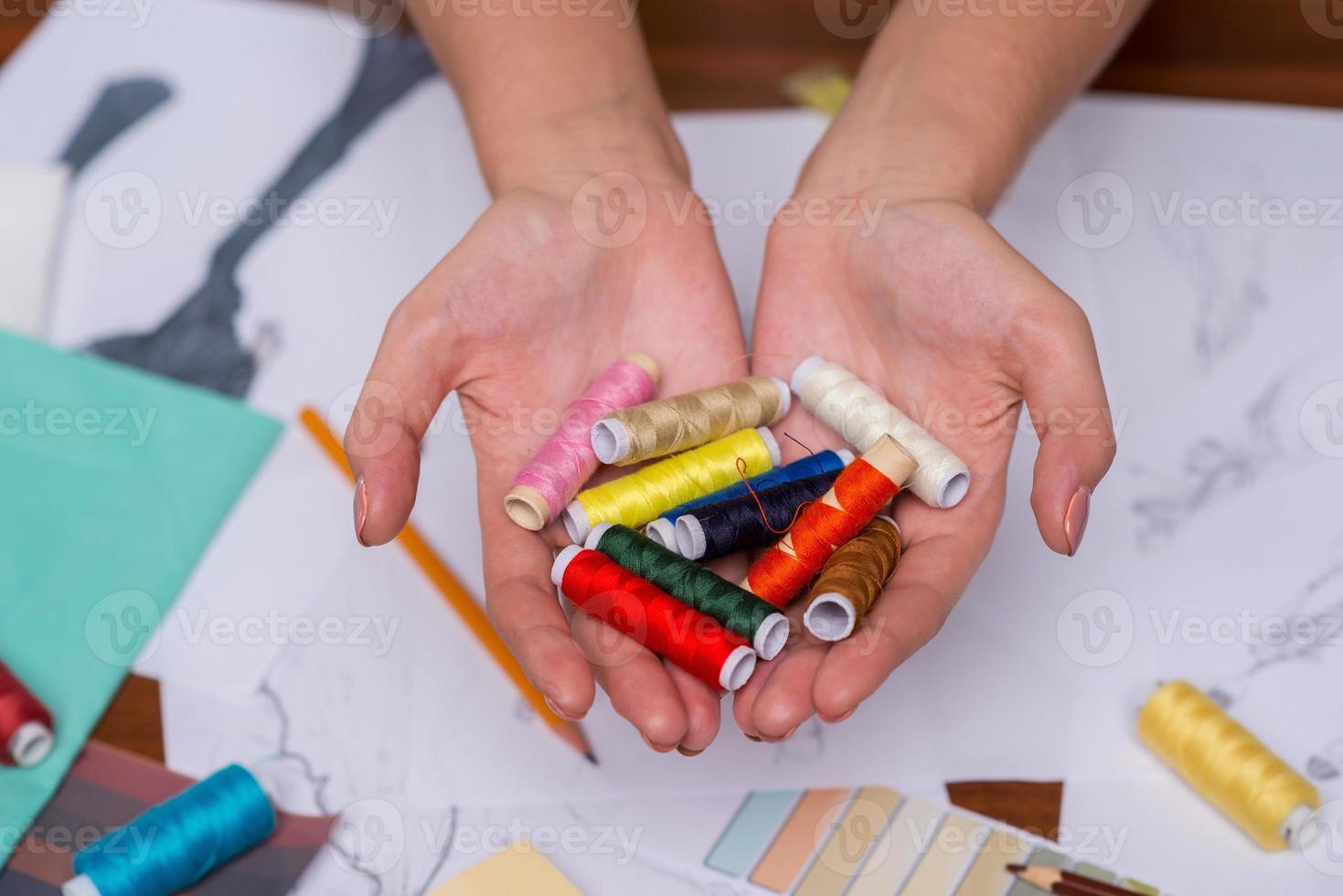 Multi colored threads in her hands. Close-up top view of woman drawing fashion sketch while sitting at her working place photo