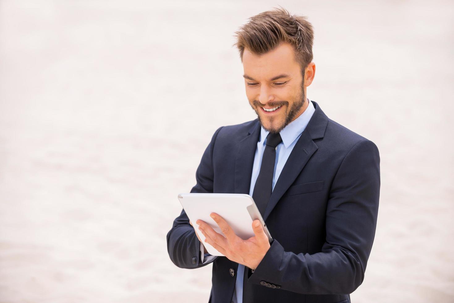 Surfing the net in desert. Cheerful young man in formalwear working on digital tablet while standing in desert photo