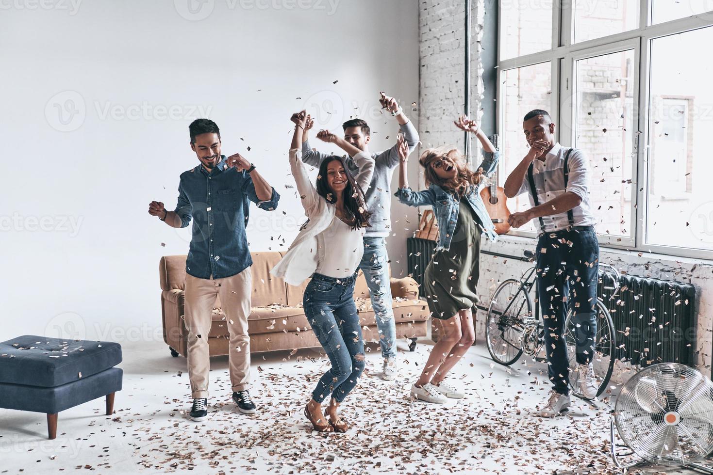 volviéndose loco. longitud completa de jóvenes felices bailando mientras pasan tiempo en casa con confeti volando por todas partes foto