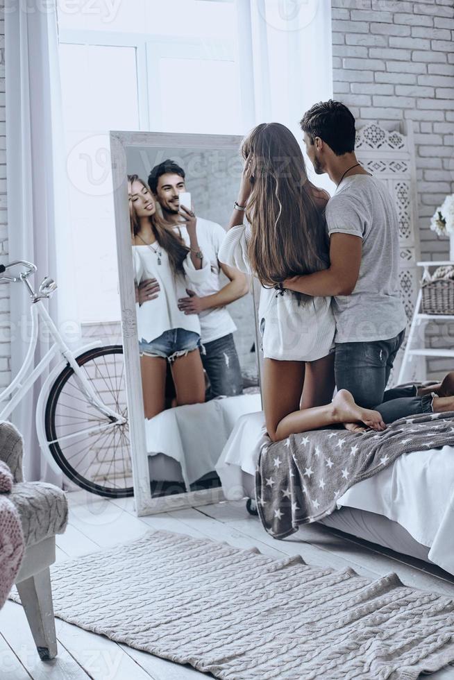 Capturing love. Rear view of young people talking selfie and smiling while looking in the mirror at home photo