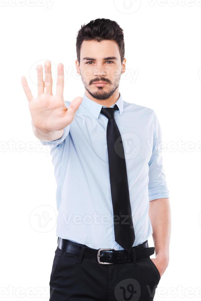 Stop it Confident young man in shirt and tie showing his palm and looking at camera while standing against white background photo