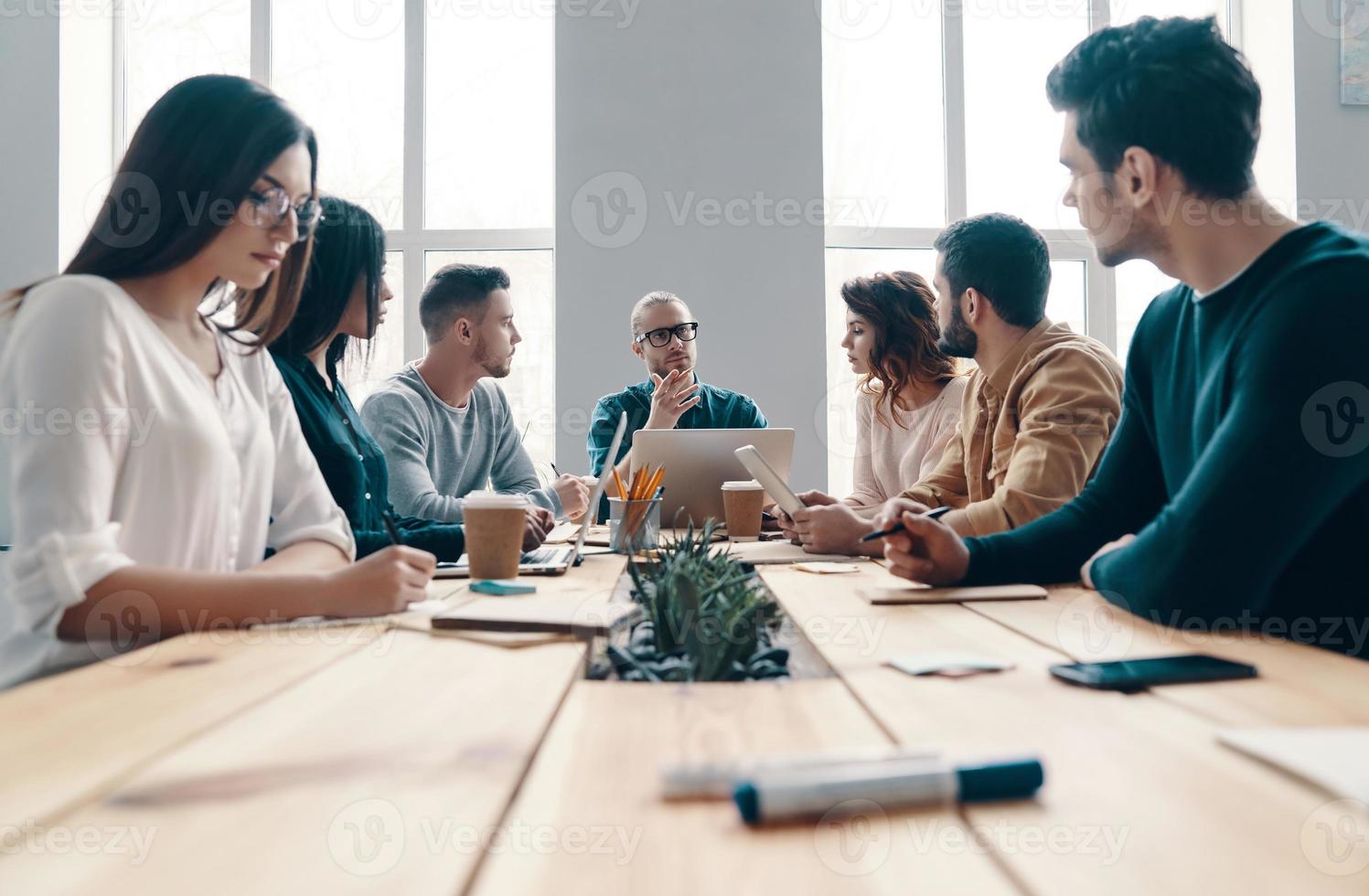 Staff meeting. Group of young modern people in smart casual wear discussing something while working in the creative office photo