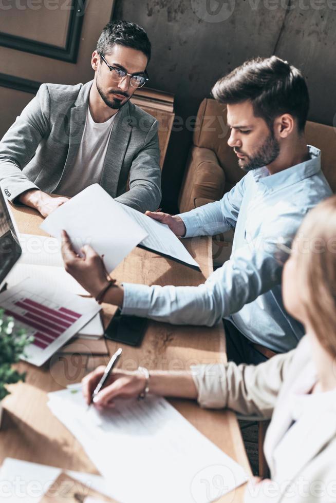 Inspired to work hard. Top view of young modern people in smart casual wear discussing business while sitting in the creative office photo