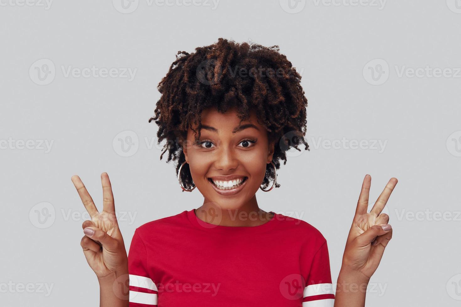 Attractive young African woman looking at camera with smile and gesturing while standing against grey background photo