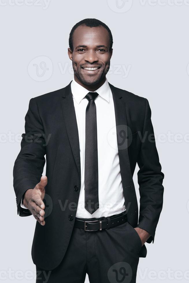 Good to see you in our team Handsome young African man in formalwear man stretching out hand for shaking and smiling while standing against grey background photo