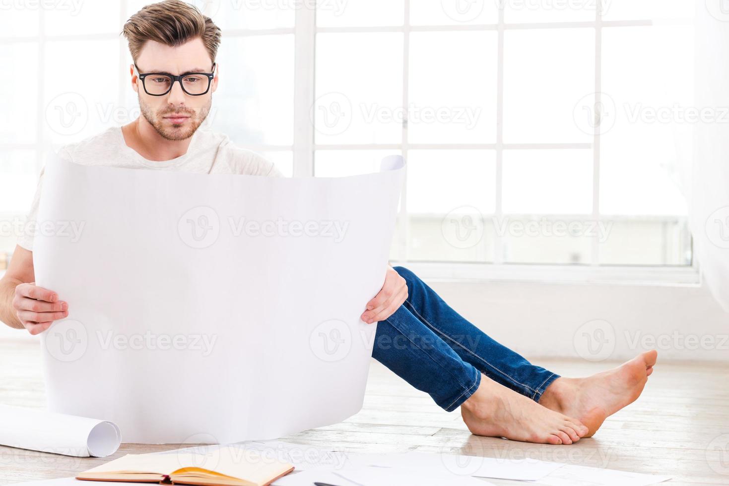 Architect working at home. Confident young man examining blueprint while sitting on the floor at home photo