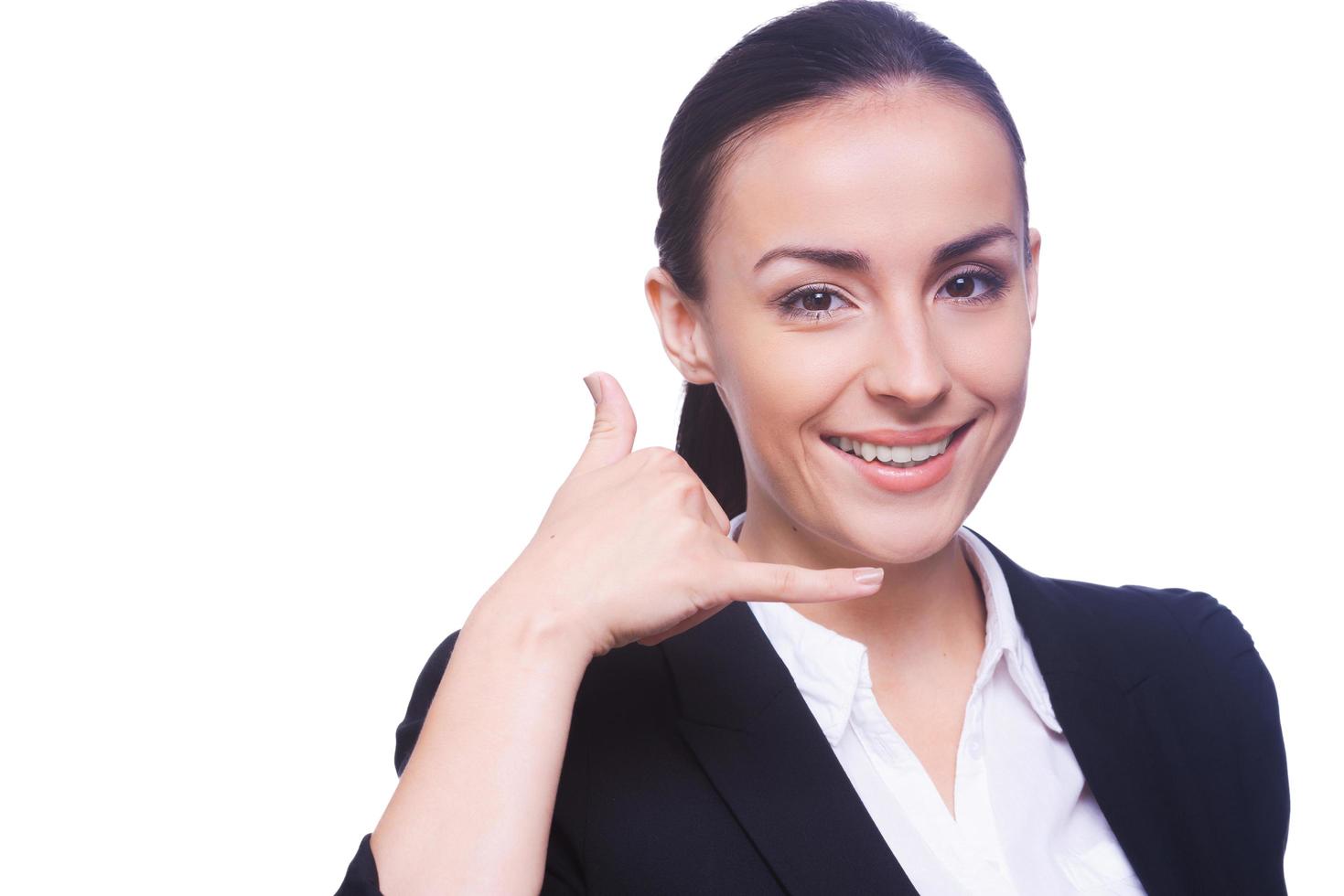 Waiting for your call. Portrait of cheerful young woman in formalwear looking at camera and gesturing mobile phone near her face while standing isolated on white photo