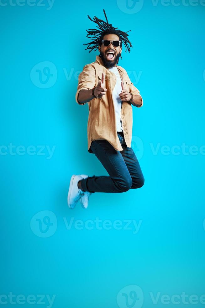 Full length of cheerful Young African man in casual wear shouting and gesturing while hovering against blue background photo