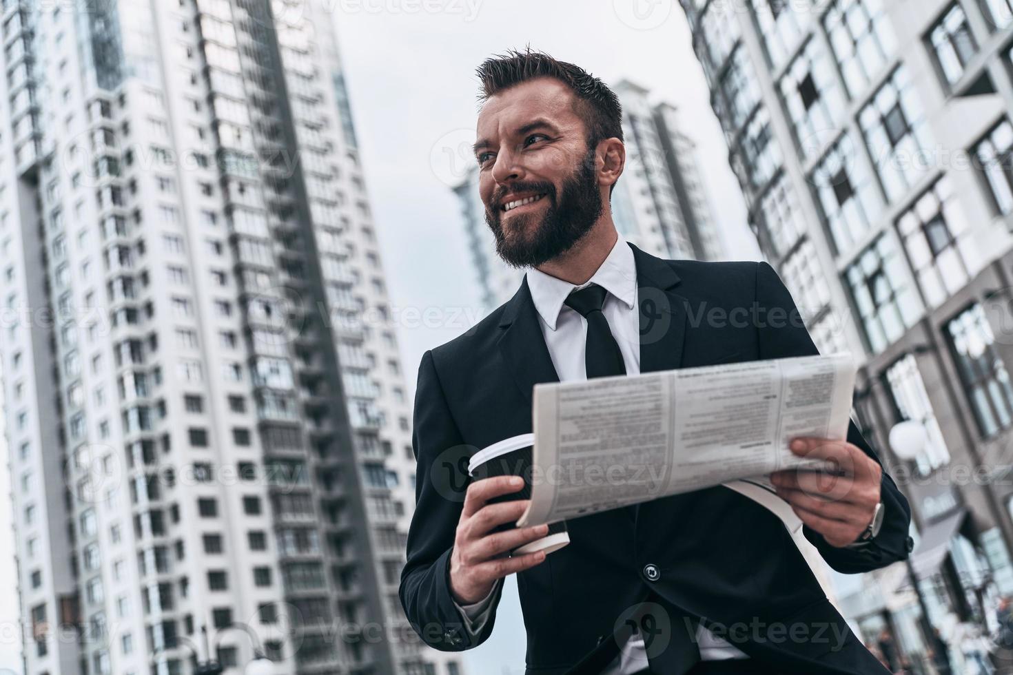 Too good to be real. Good looking young man in full suit looking away and smiling while sitting outdoors photo