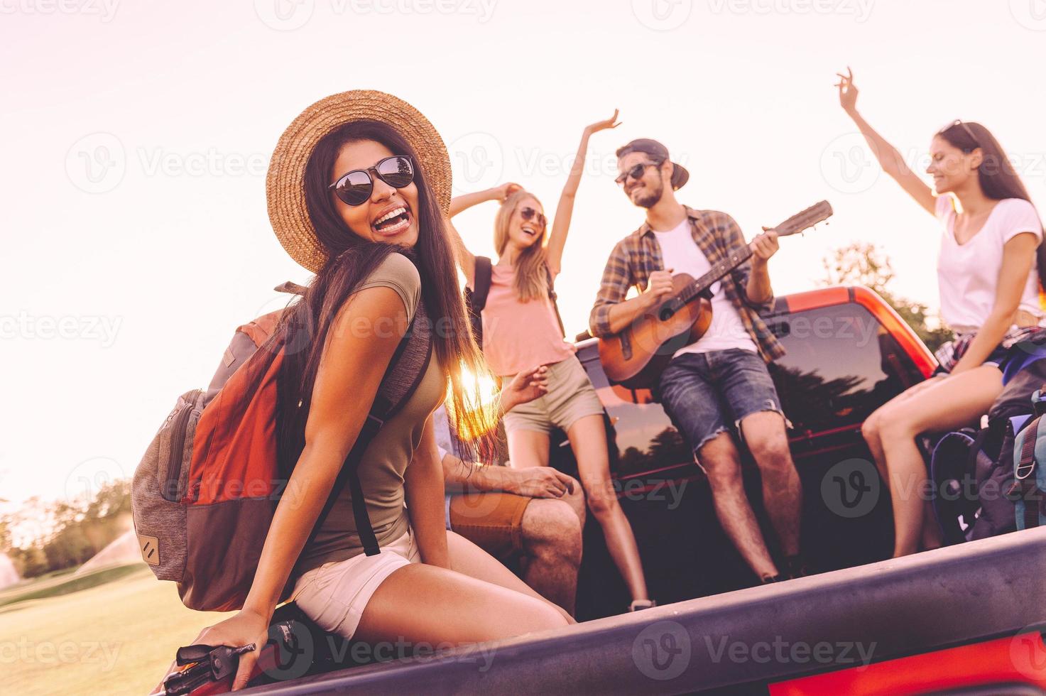 disfrutando de un viaje por carretera con los mejores amigos. grupo de jóvenes alegres bailando y tocando la guitarra mientras disfrutan juntos de su viaje por carretera en un camión de recogida foto