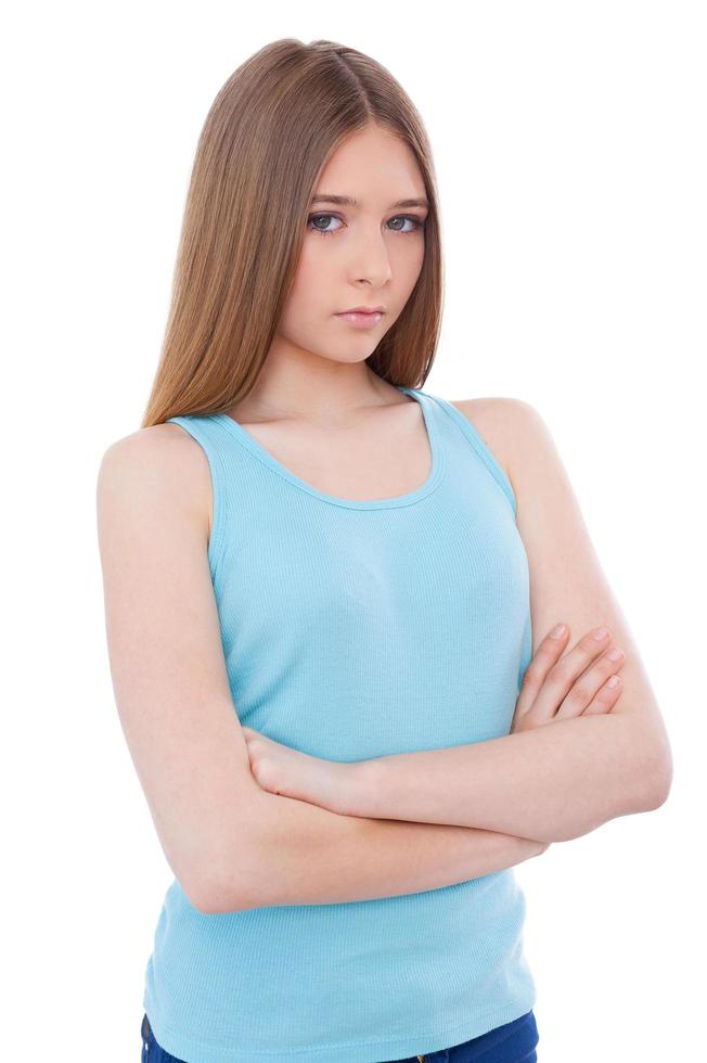 Difficult age. Sad young teenage girl keeping arms crossed and looking at camera while standing isolated on white photo