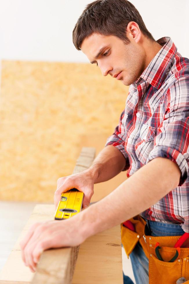 Everything should be perfect. Confident young handyman working with wood in workshop photo