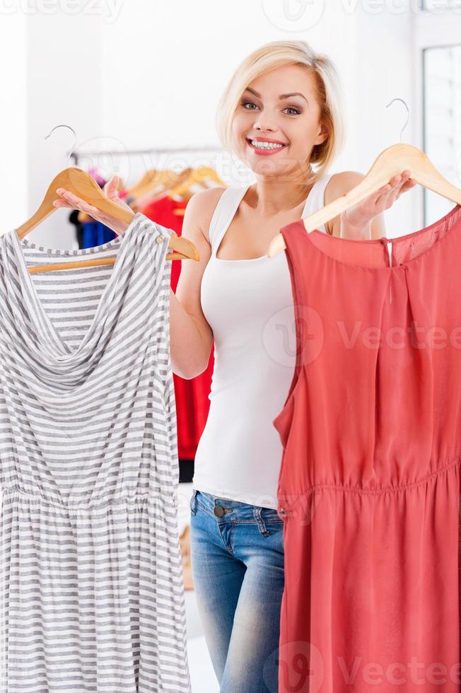 So hard to choose Attractive young blond hair woman holding two dresses and looking at camera photo