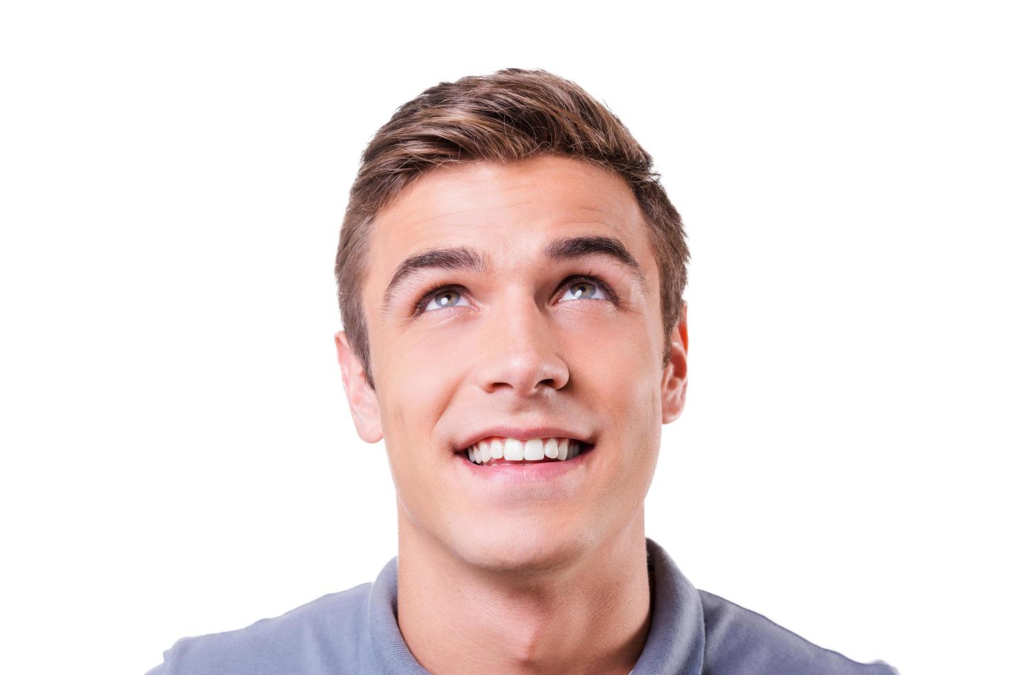 Curious young man. Cheerful young man looking up and smiling while standing isolated on white background photo