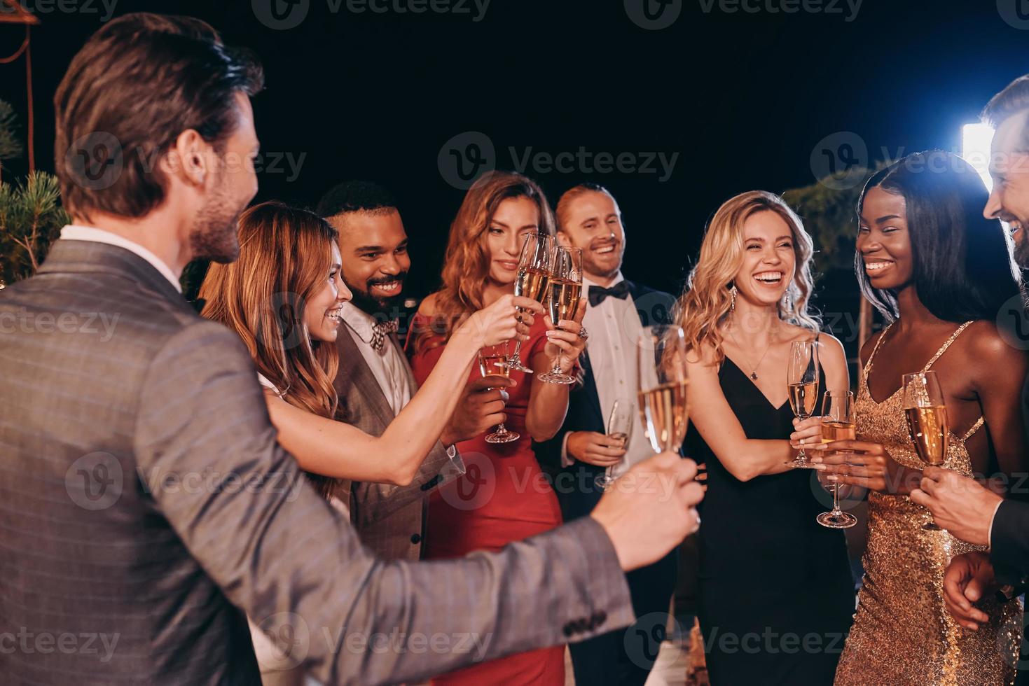 grupo de personas en ropa formal comunicándose y sonriendo mientras pasan tiempo en una fiesta de lujo foto