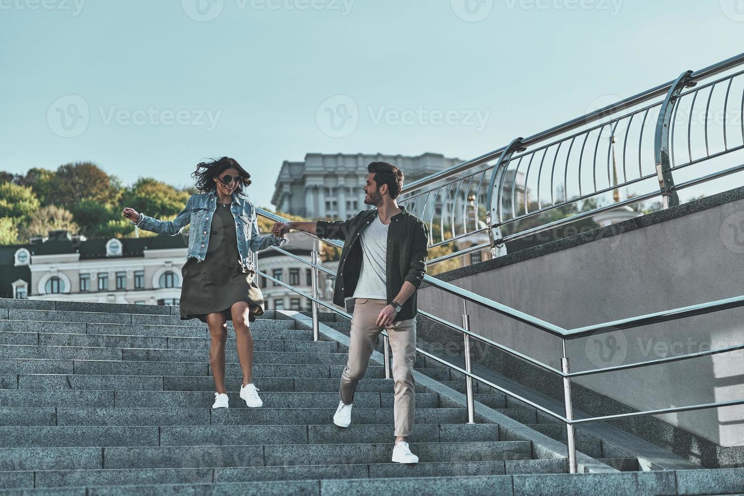 Happy to be together. Full length of handsome man and young attractive woman holding hands while walking down the stairs outdoors photo