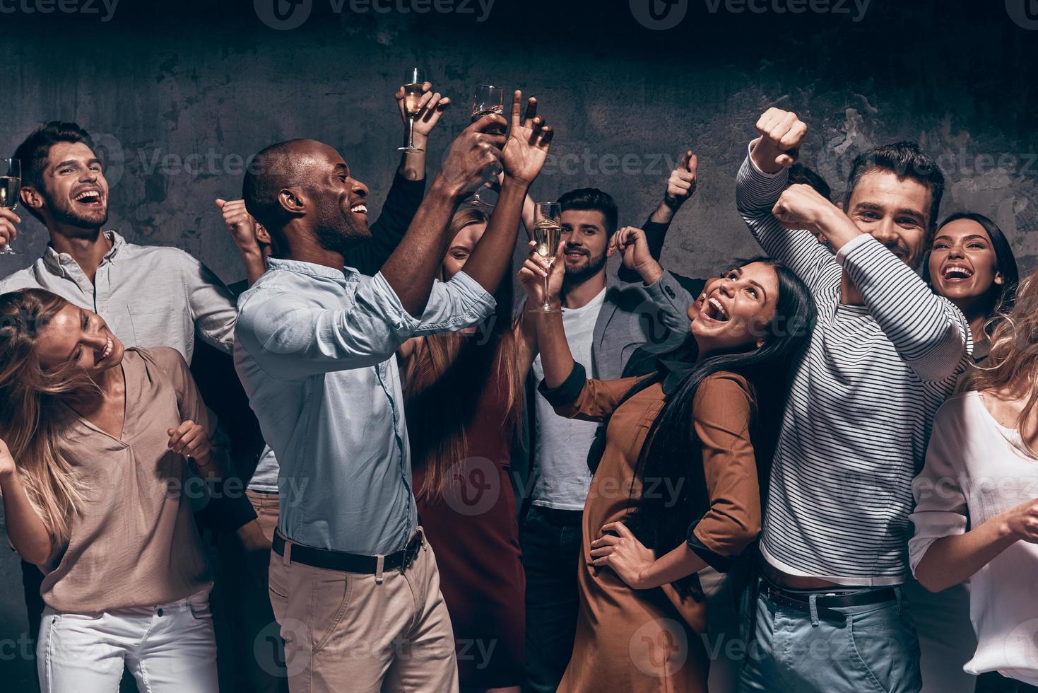 disfrutando de una fiesta increíble. grupo de hermosos jóvenes bailando con flautas de champán y luciendo felices foto