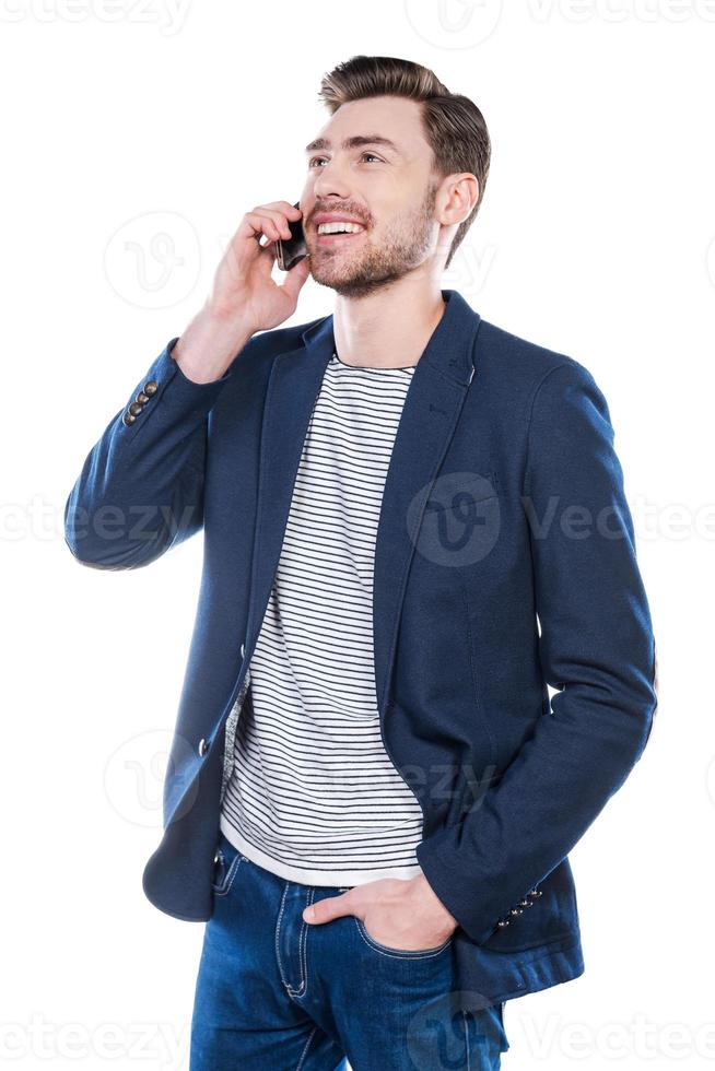 Good talk with friend. Handsome young man talking on the mobile phone and smiling while standing against white background photo