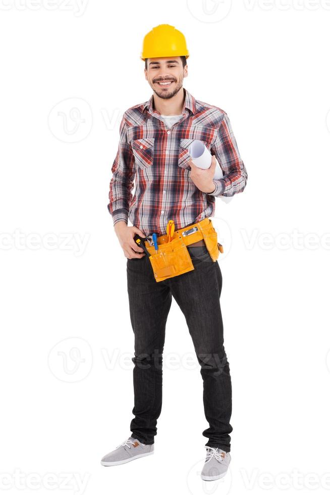 Confident repairman. Full length of confident young male carpenter in hardhat holding blueprint and smiling while standing against white background photo