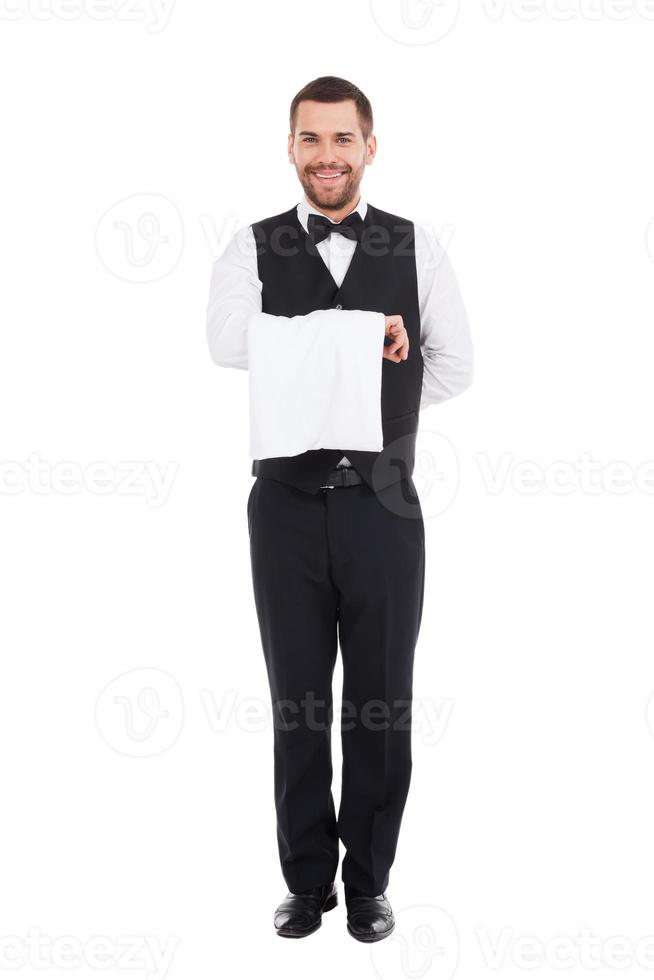 camarero confiado. longitud total de un camarero confiado que lleva una toalla en la mano y sonríe mientras está de pie contra el fondo blanco foto