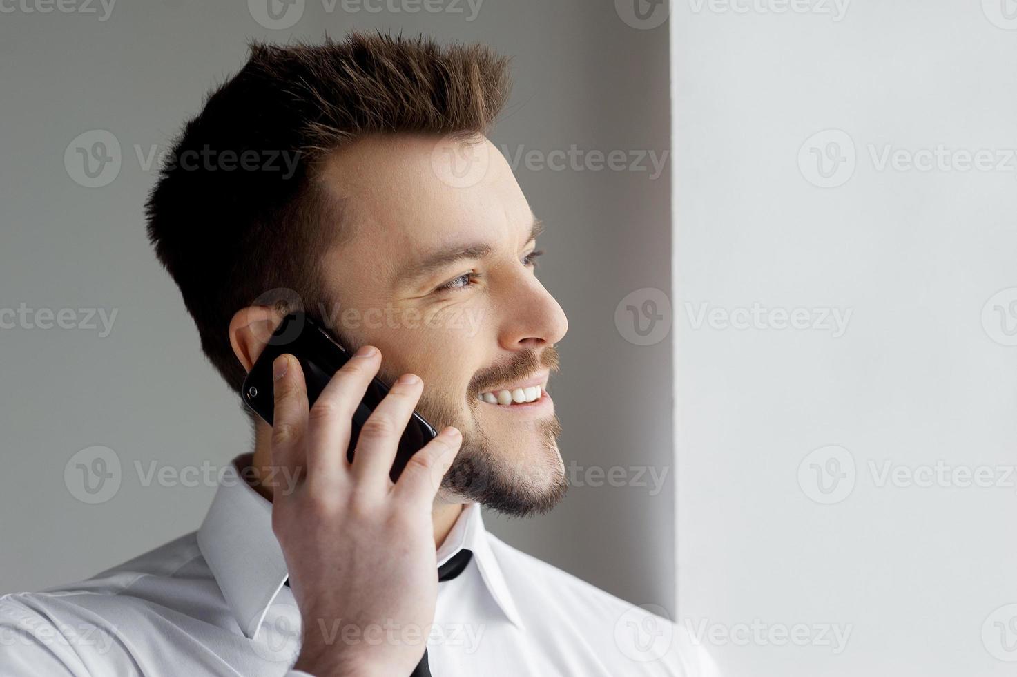 Good talk. Handsome young man in formalwear talking on the mobile phone and smiling photo