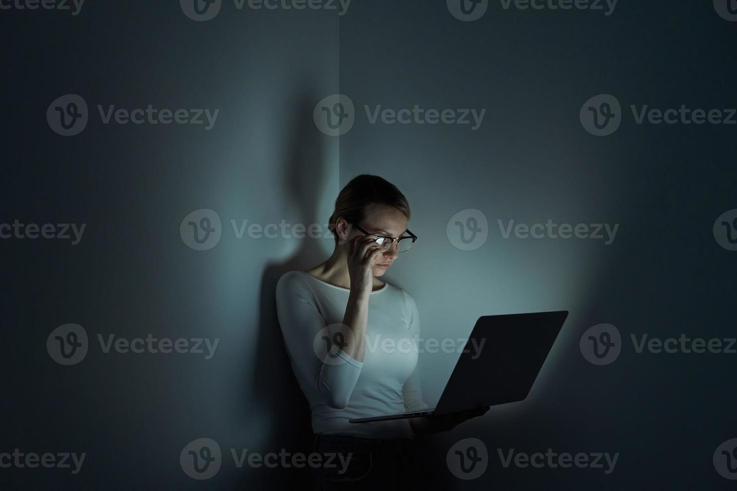 mujer joven confiada que trabaja en la computadora portátil contra una pared oscura foto
