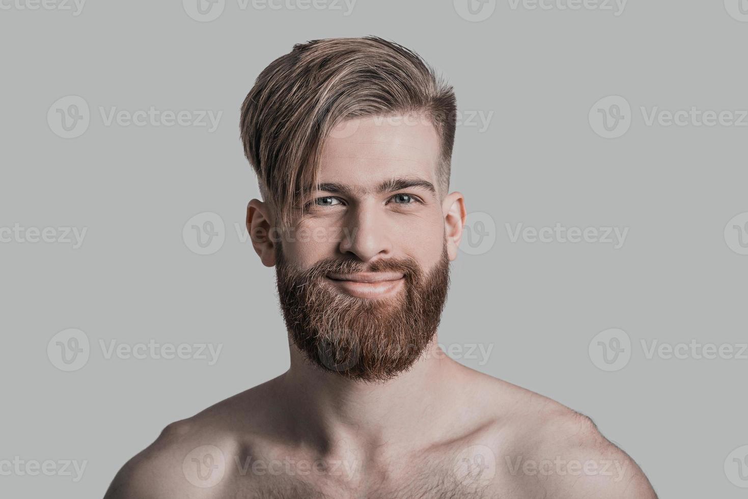 Smiling handsome. Portrait of handsome man looking at camera and smiling while standing against grey background photo