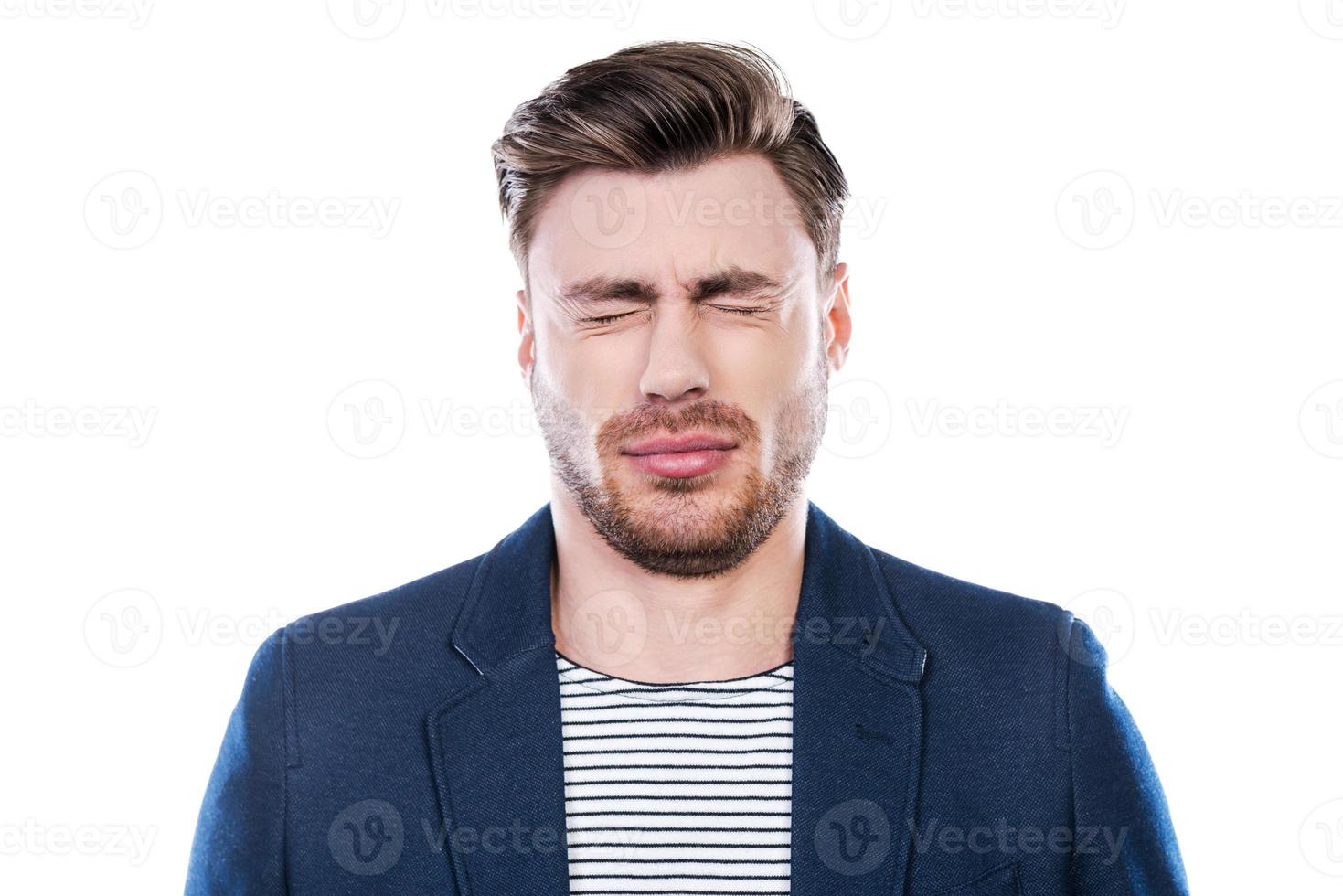 Oh no Portrait of young man expressing negativity and keeping eyes closed while standing against white background photo