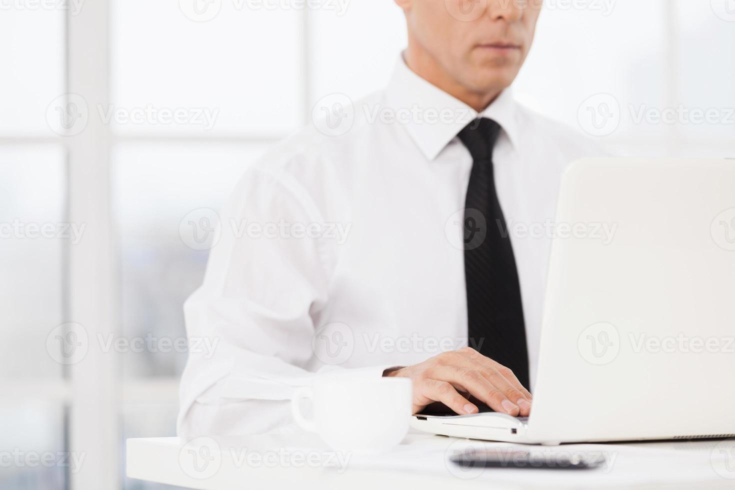 Businessman at working place. Cropped image of man in shirt and tie using computer while sitting at his working place photo