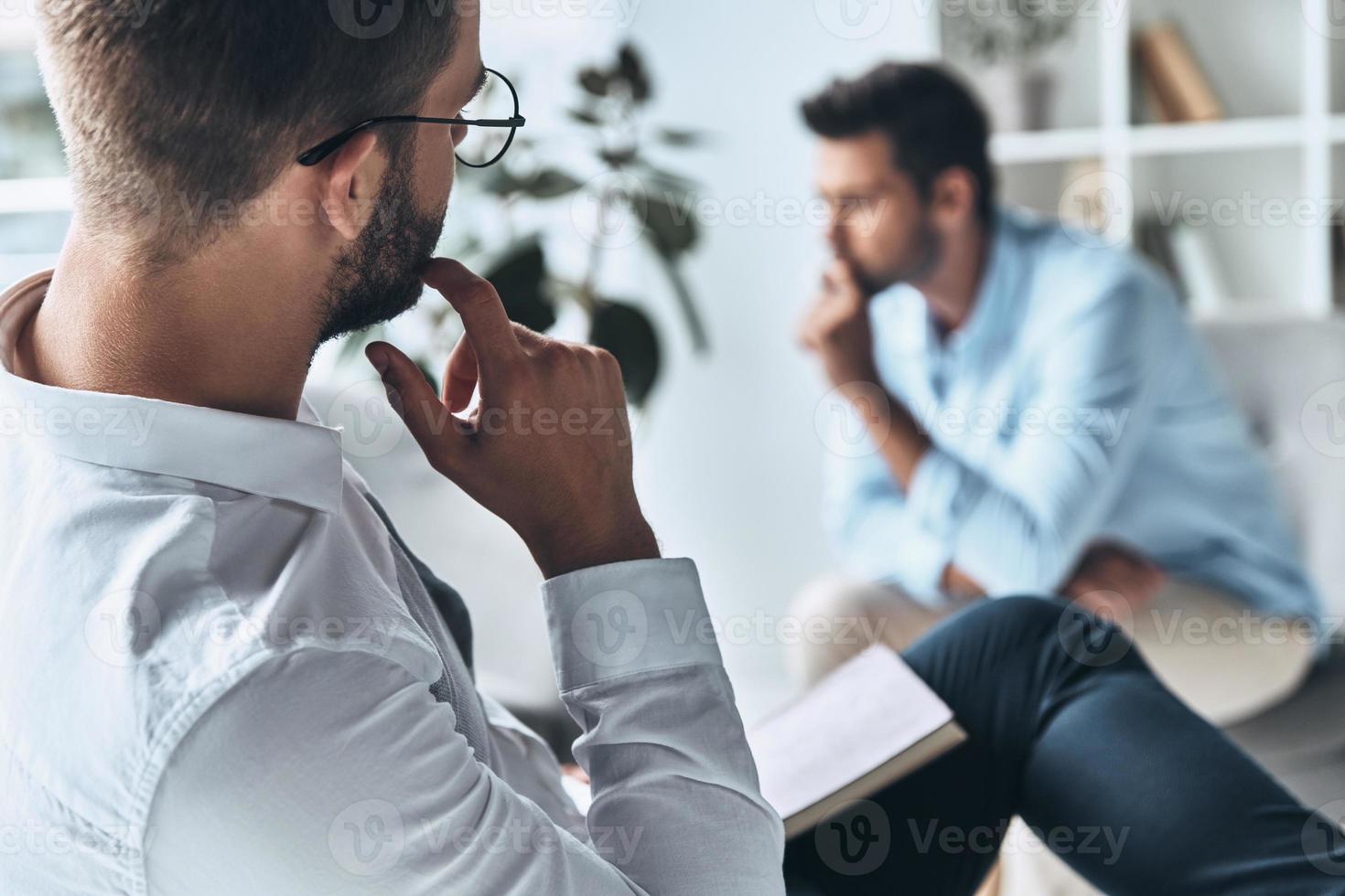 Need mental help. Young frustrated man solving his mental problems while having therapy session with psychologist photo