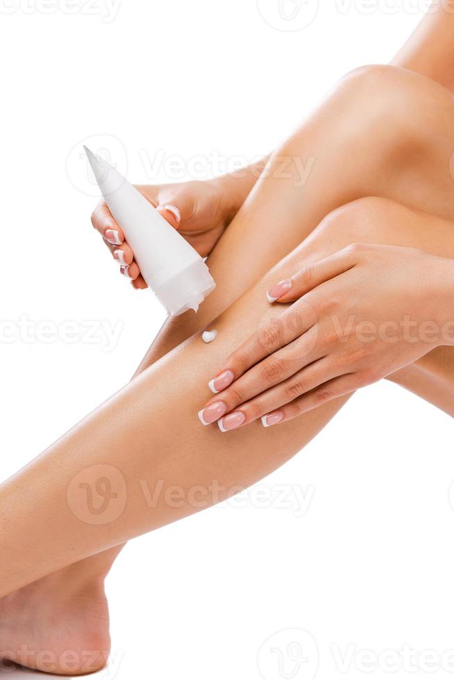 Important hydration of skin. Cropped picture of a beautiful young woman applying body lotion on her legs while sitting against white background photo