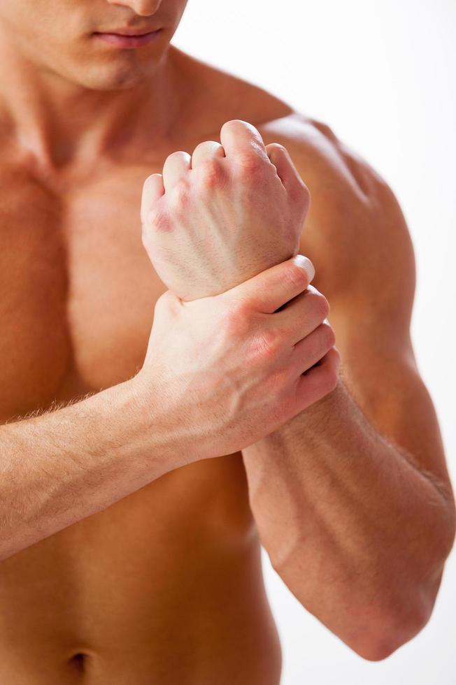 Pain in wrist. Close-up of young muscular man touching his wrist while standing against white background photo