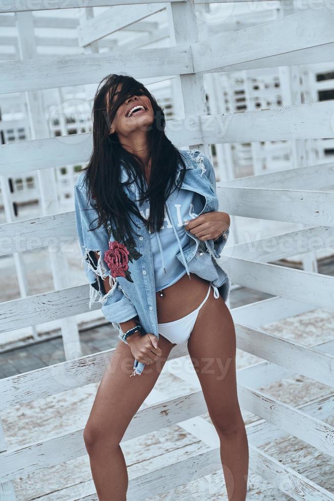 sintiéndose libre de expresar su sensualidad. atractiva joven mujer de raza mixta en pantalones vaqueros sonriendo mientras está de pie al aire libre foto