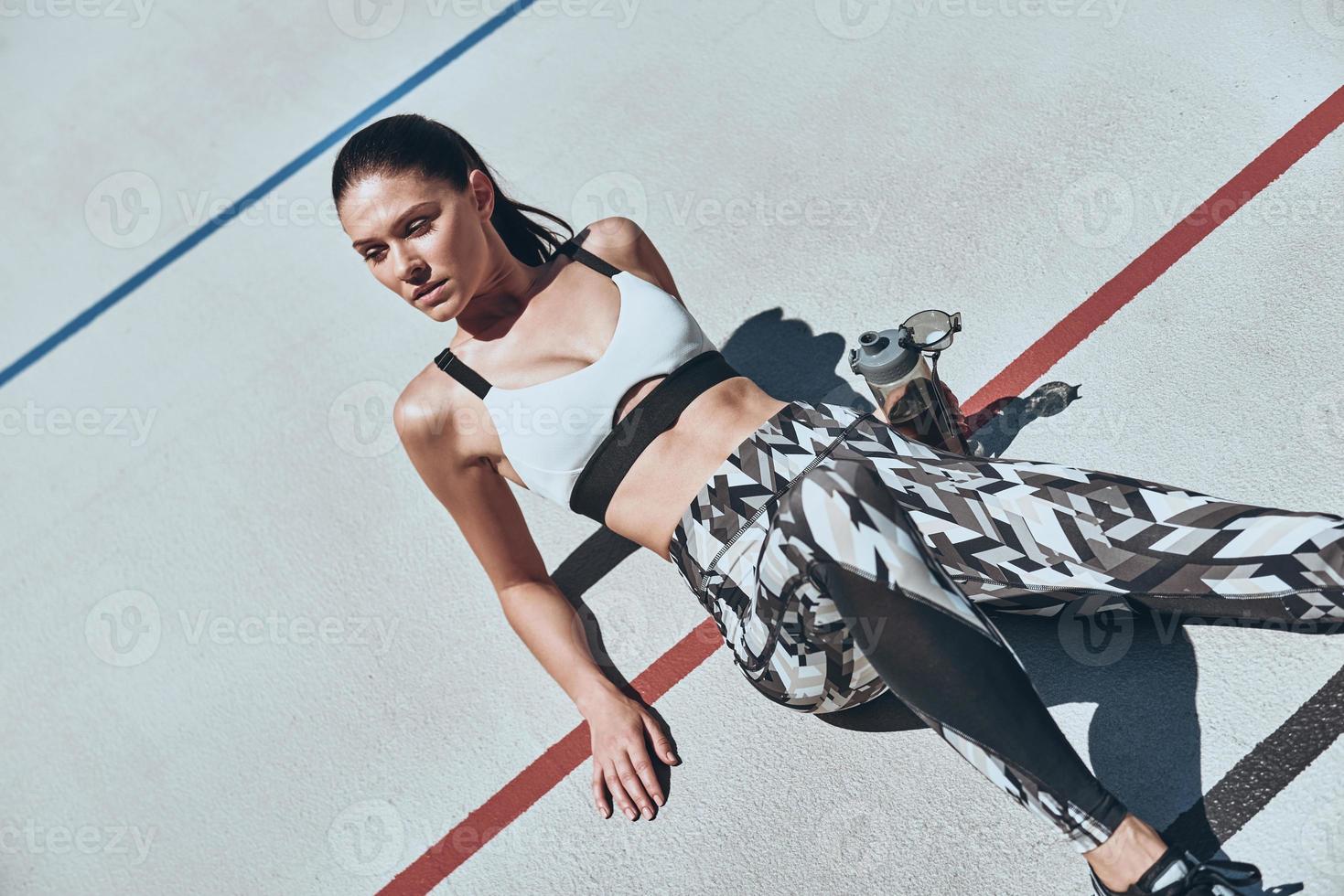 Time for a little break. Top view of young woman in sports clothing relaxing while lying on the running track outdoors photo