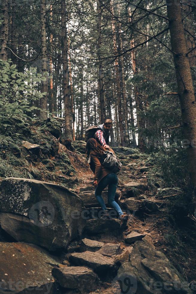 Dealing with difficulties. Full length of young couple holding hands and moving up while hiking together in the woods photo