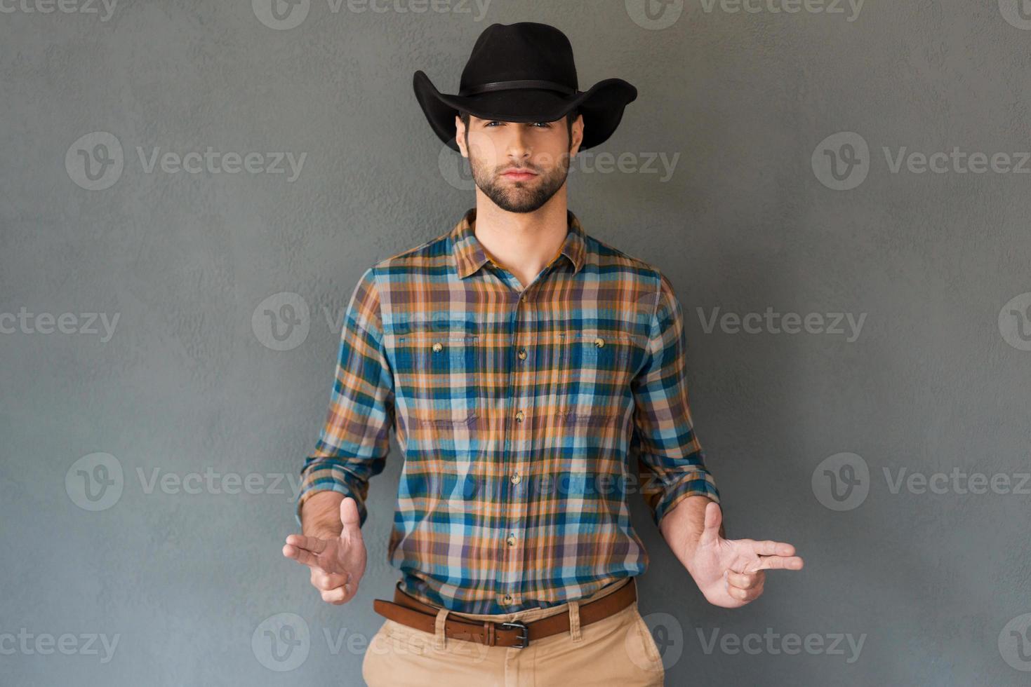 Hands up Handsome young man wearing cowboy hat and gesturing while standing against grey background photo
