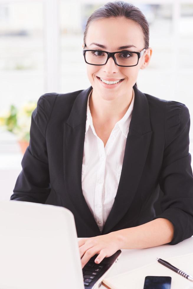 empresaria en el trabajo. mujer de negocios joven que usa la computadora y sonríe mientras está sentada en su lugar de trabajo foto