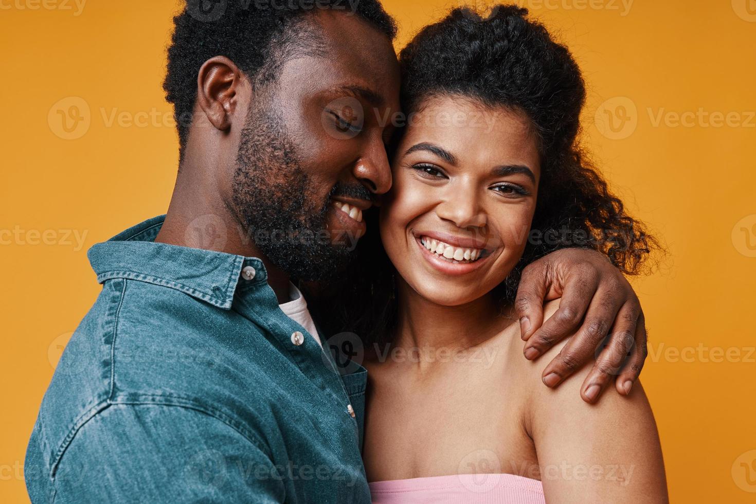 Beautiful young African couple hugging and smiling while standing against yellow background photo