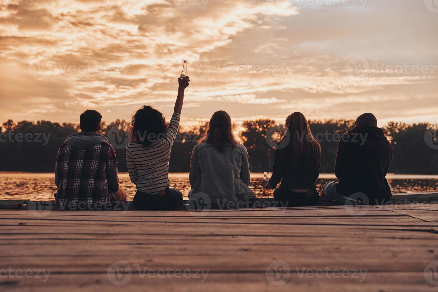 grupo de jóvenes con ropa informal tomándose selfie y sonriendo mientras disfrutan de una fiesta en la playa cerca de la fogata foto