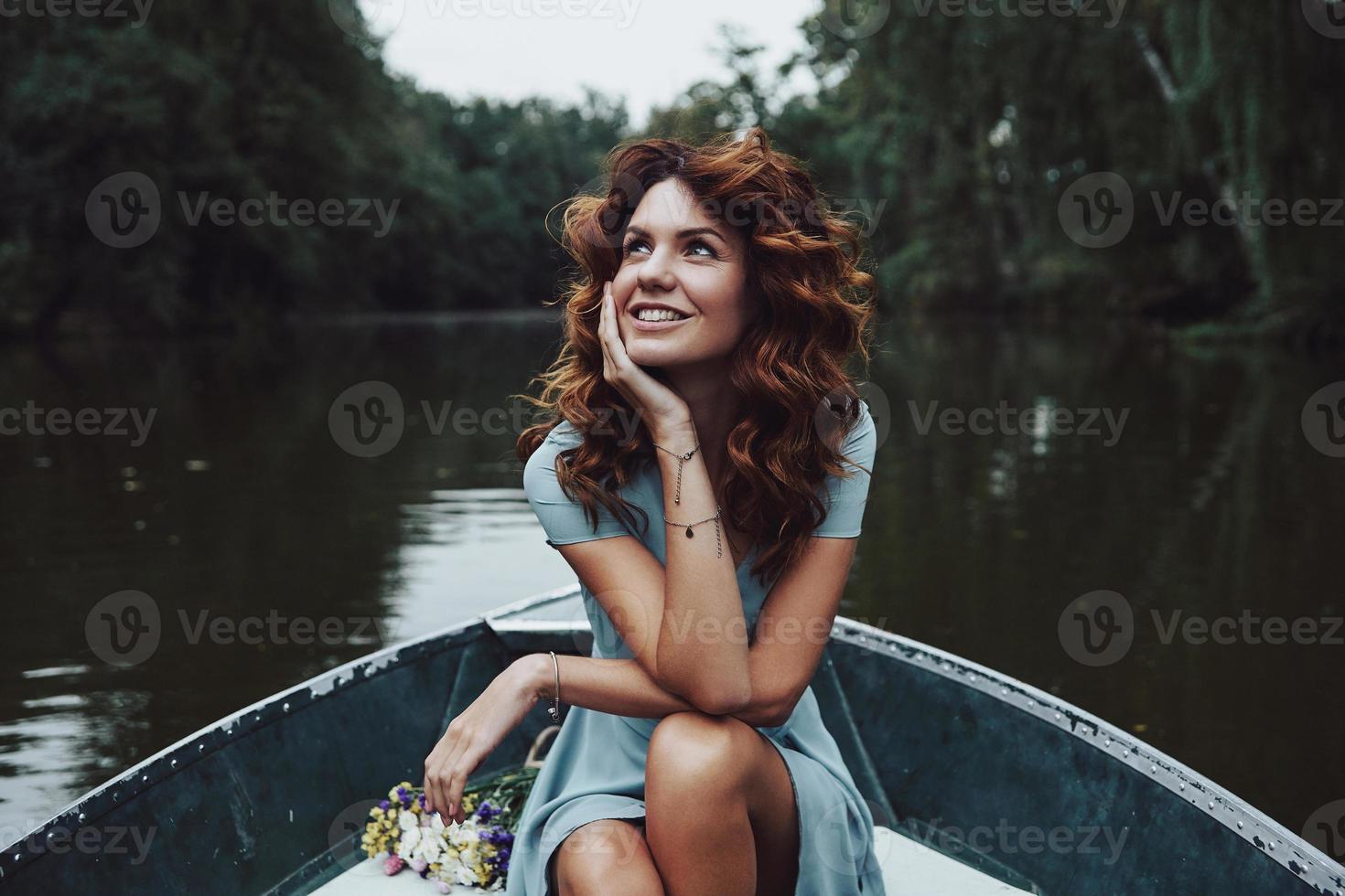 simplemente feliz. bella joven con un vestido elegante mirando hacia otro lado y sonriendo mientras se sienta en el bote foto