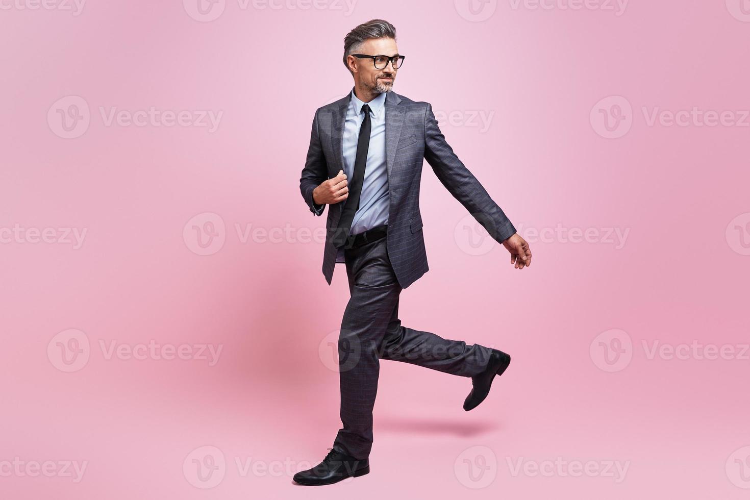Confident mature man in full suit walking against pink background photo