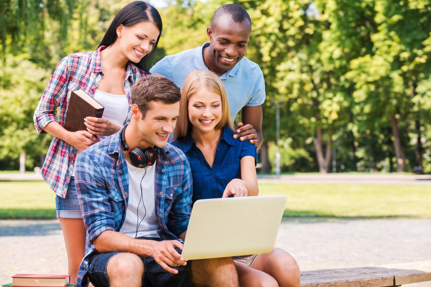 pasando tiempo juntos. cuatro jóvenes felices discutiendo algo y mirando la laptop mientras se sientan juntos al aire libre foto