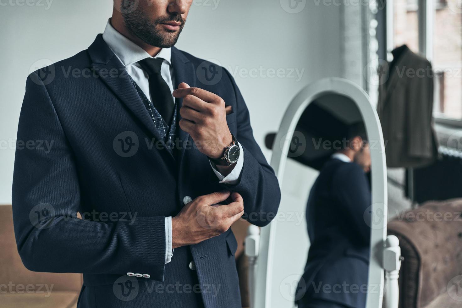 Perfect style. Close up of young man in full suit adjusting sleeve while standing indoors photo