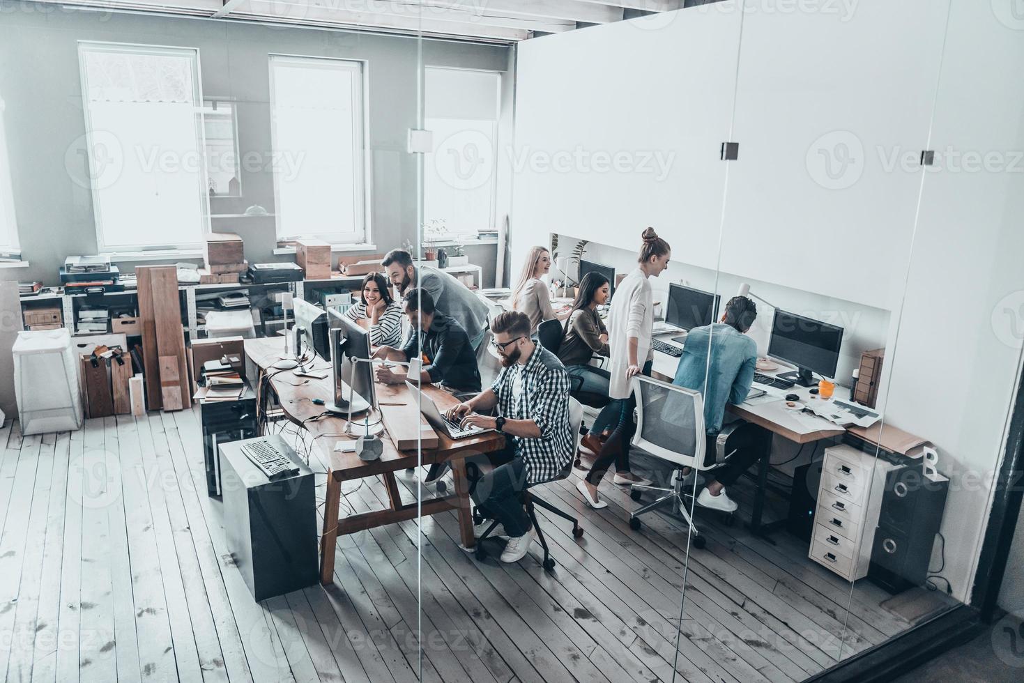 Concentrated at work.  Top view of young modern people in casual wear concentrating at their projects while working together behind the glass wall in the creative office photo