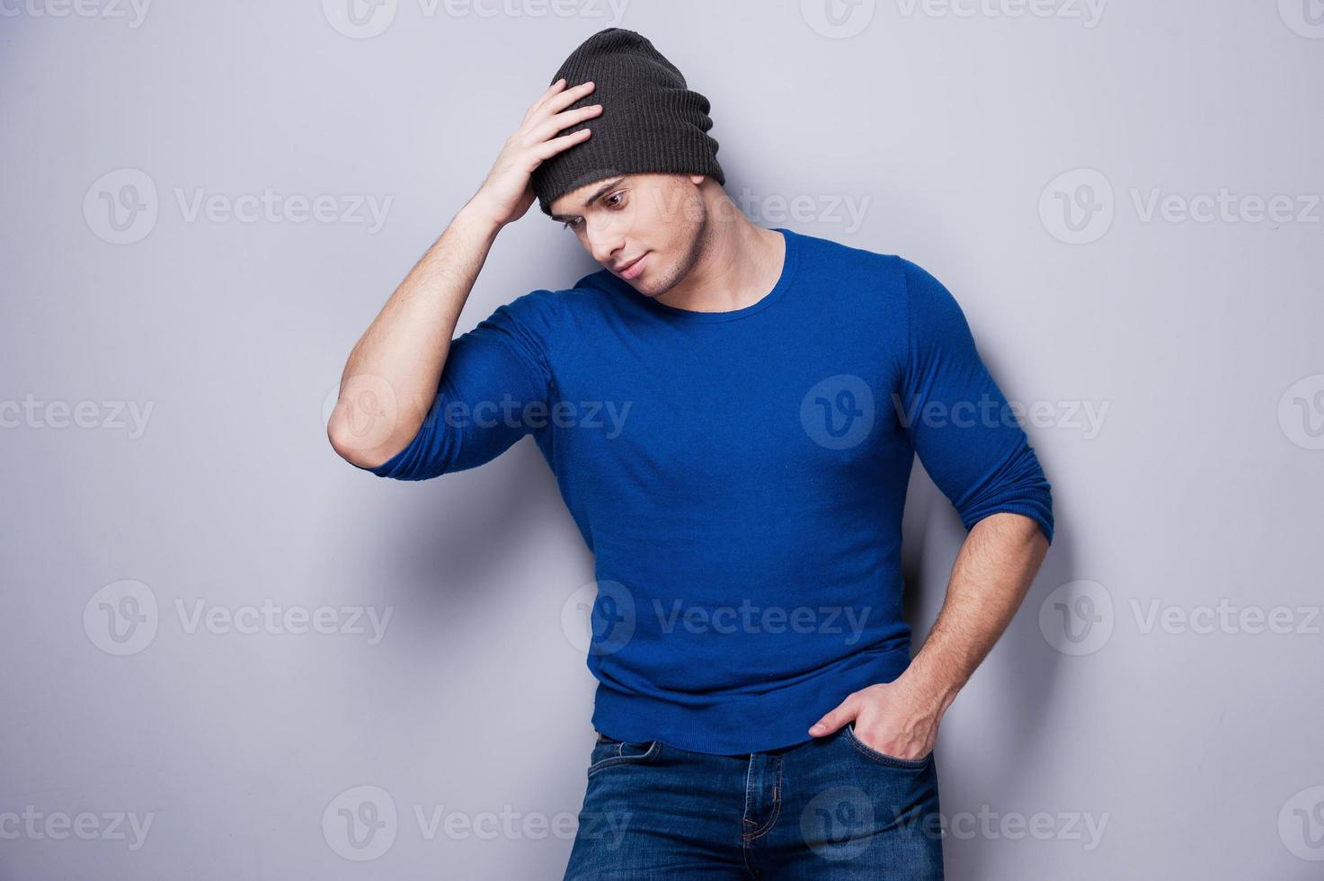 Real macho. Thoughtful young man holding hand on his head while standing against grey background photo