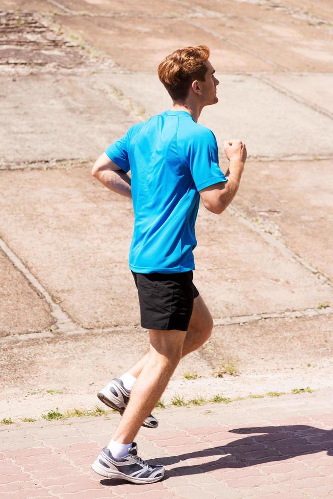 Enjoying a morning run.  Side view of young man running along the road photo