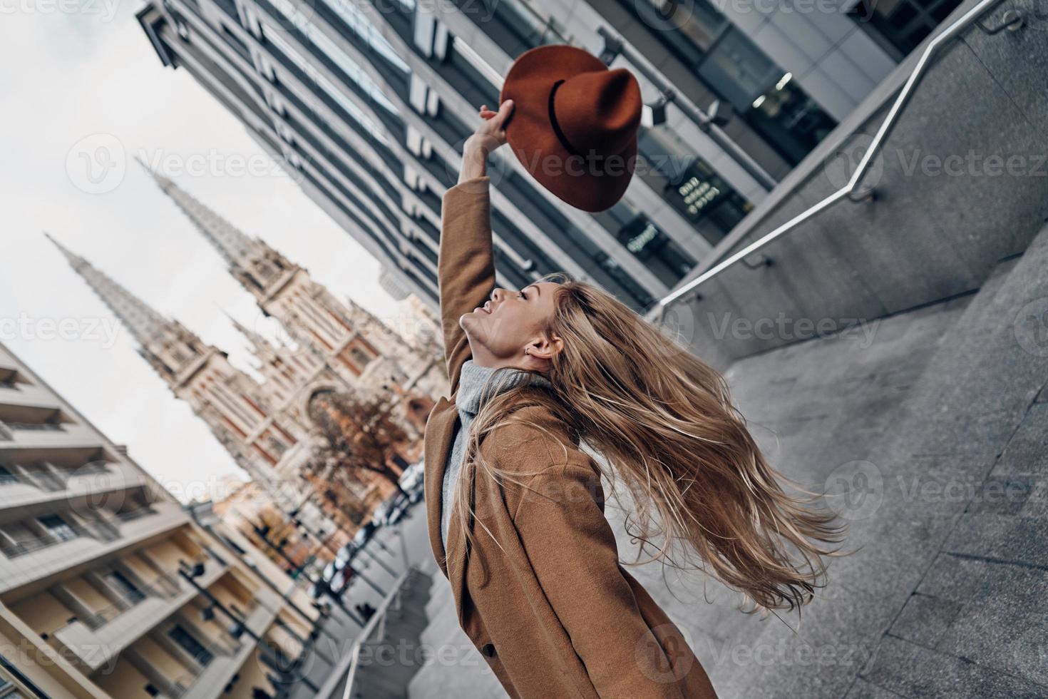 Beauty and style. Attractive young woman holding hat and smiling while spending carefree time in the city photo