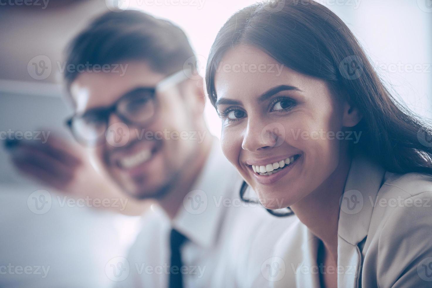 Working together with joy. Close-up part of two coworkers looking at camera with smile while sitting at office photo
