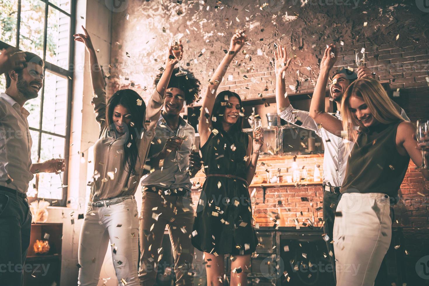 Enjoying cool party. Group of happy young people throwing confetti and jumping while enjoying home party on the kitchen photo